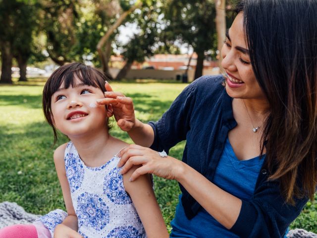 Woman putting sunscreen on daughter's face in park