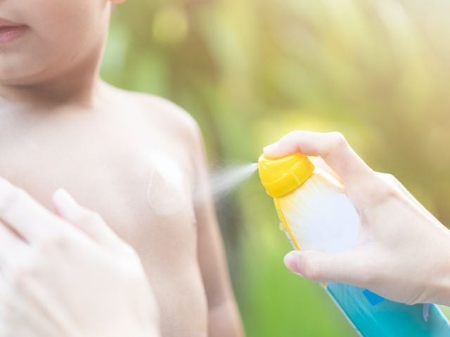 Child being sprayed with sunscreens
