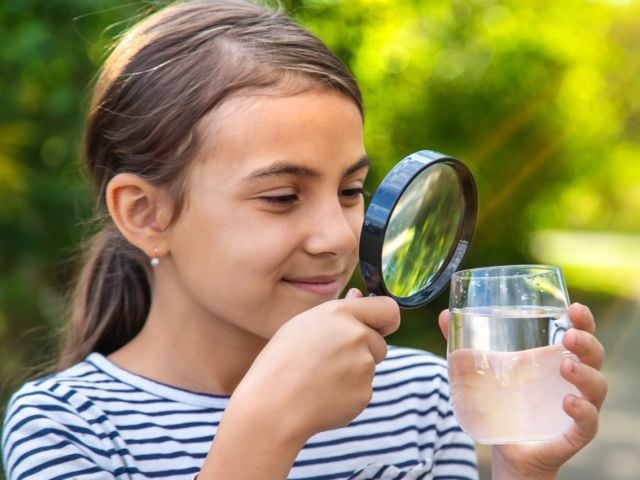 Young girl looking at a glass of water through magnifying glass